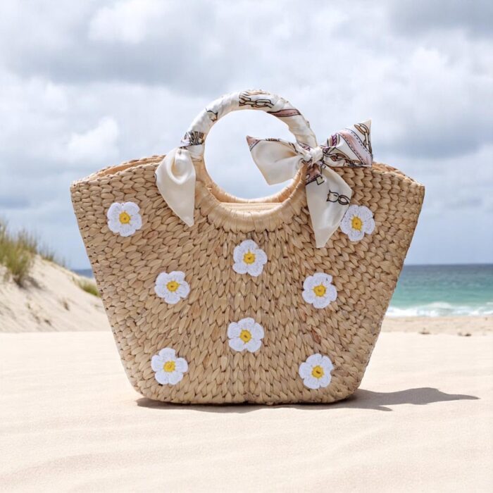 Floral straw beach tote with white daisy embroidery, circular handles wrapped in ivory bows