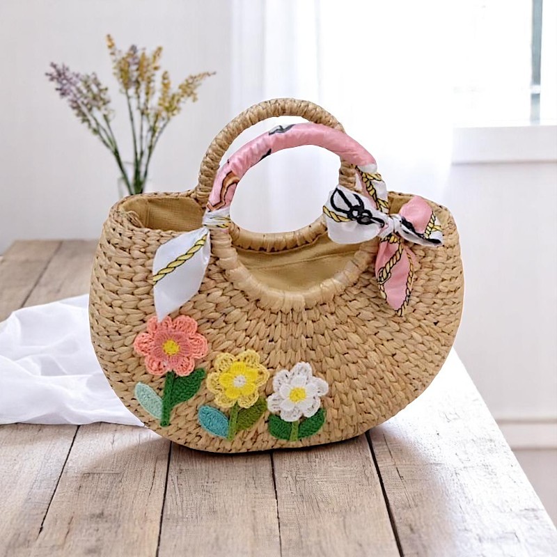 Handmade water hyacinth straw bag with floral crochet embroidery, scarf-wrapped handles, and rounded silhouette